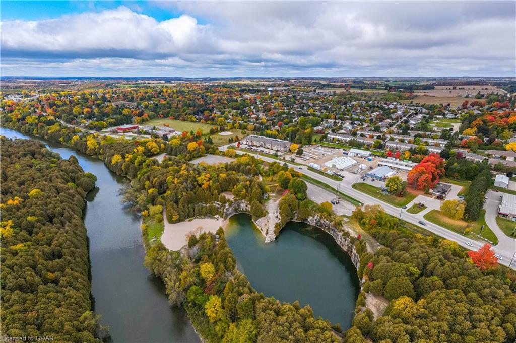 Aerial view of Elora showing the river winding past a quarry lake, dense autumn trees, and a small town under a cloudy sky.
